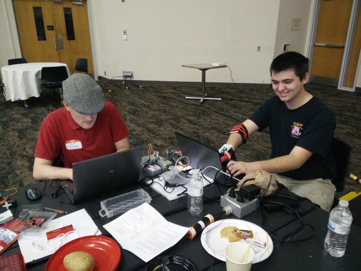 Two people at a table with laptops, a breadboard and electronics between them.